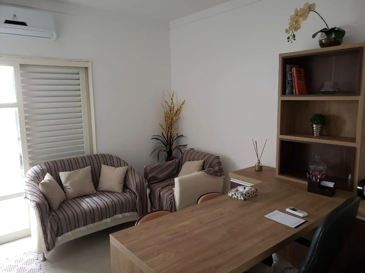 Sala com sofás listrados, mesa de madeira e estante, para as conversas com as famílias.
